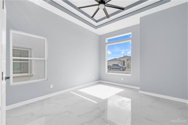 unfurnished room with marble finish floor, a tray ceiling, a ceiling fan, and baseboards