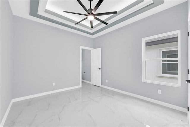 empty room featuring marble finish floor, baseboards, a raised ceiling, and a ceiling fan