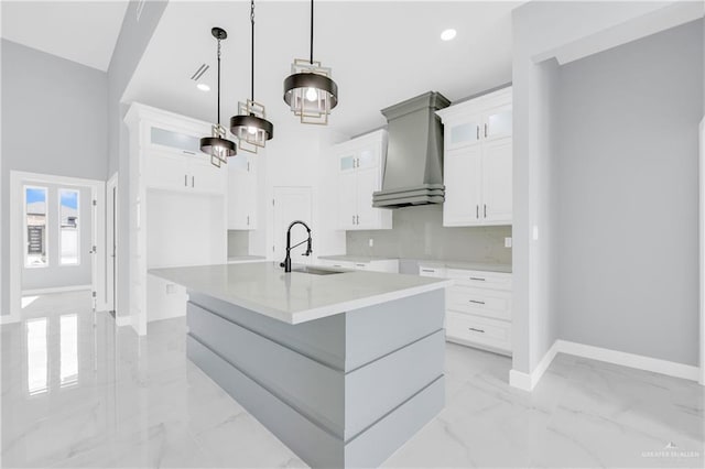 kitchen featuring premium range hood, white cabinets, decorative light fixtures, and a large island with sink