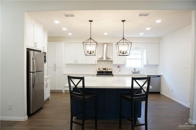 kitchen featuring wall chimney exhaust hood, a center island, white cabinetry, and appliances with stainless steel finishes