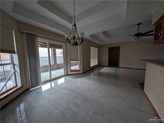 unfurnished dining area with ceiling fan with notable chandelier, a healthy amount of sunlight, a water view, and a tray ceiling