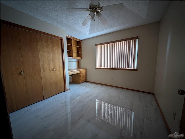 unfurnished bedroom featuring a textured ceiling, built in desk, and ceiling fan