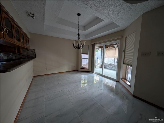 unfurnished dining area featuring a raised ceiling, a textured ceiling, and a notable chandelier