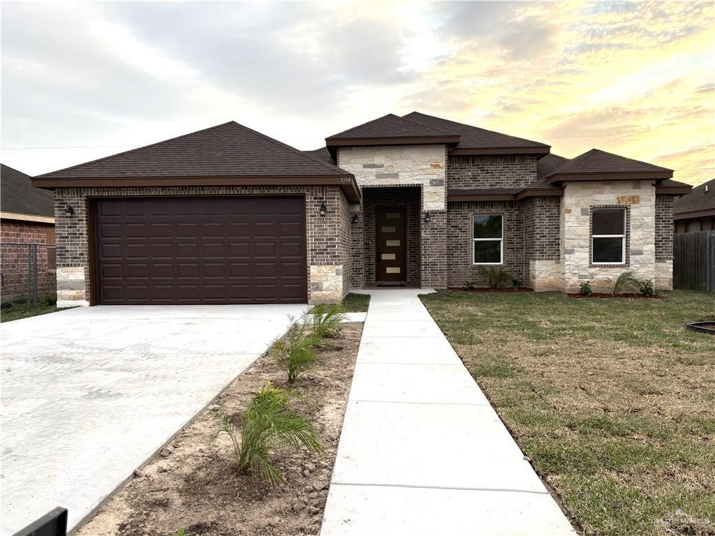 prairie-style house with an attached garage, brick siding, fence, concrete driveway, and a front yard