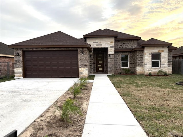 prairie-style house with an attached garage, brick siding, fence, concrete driveway, and a front yard