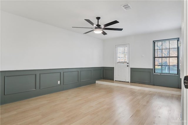 unfurnished room with visible vents, light wood-type flooring, ceiling fan, and a wainscoted wall