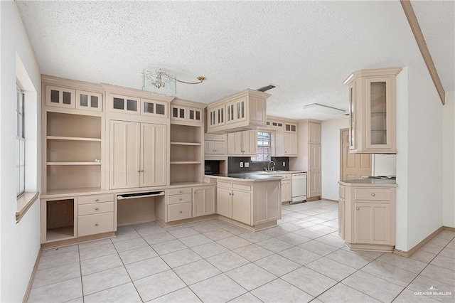 kitchen with sink, white dishwasher, built in desk, a textured ceiling, and cream cabinetry