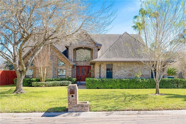 french country inspired facade with french doors, brick siding, roof with shingles, fence, and a front lawn