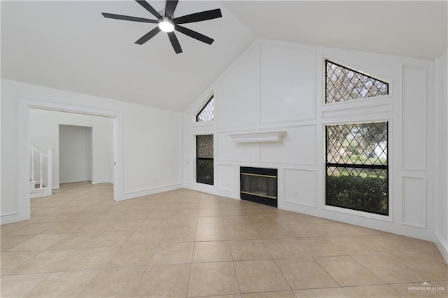 unfurnished living room featuring light tile patterned floors, high vaulted ceiling, a ceiling fan, baseboards, and a glass covered fireplace