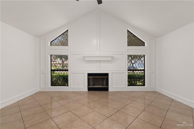 unfurnished living room with light tile patterned floors, high vaulted ceiling, a decorative wall, and a glass covered fireplace