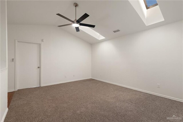 carpeted empty room featuring baseboards, vaulted ceiling with skylight, visible vents, and a ceiling fan