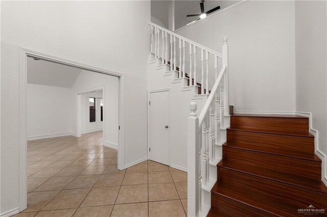 stairs featuring a towering ceiling, tile patterned flooring, a ceiling fan, and baseboards