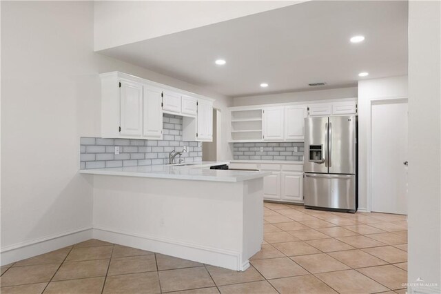 kitchen with light countertops, a peninsula, stainless steel fridge, and light tile patterned flooring