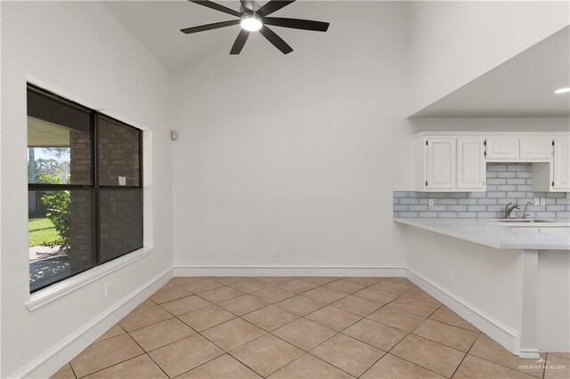 unfurnished dining area with ceiling fan, lofted ceiling, light tile patterned flooring, a sink, and baseboards