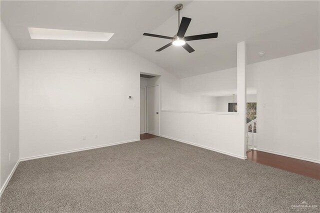 empty room with lofted ceiling with skylight, ceiling fan, baseboards, and carpet