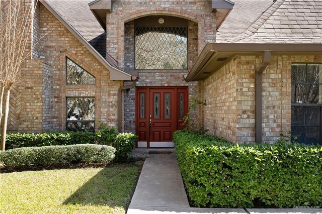 doorway to property featuring brick siding and roof with shingles