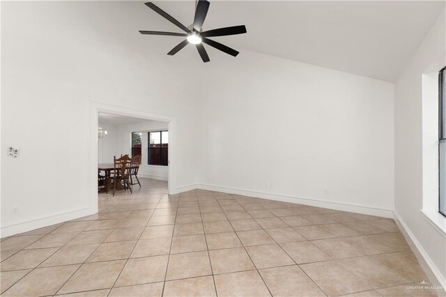 empty room featuring ceiling fan with notable chandelier, high vaulted ceiling, light tile patterned floors, and baseboards