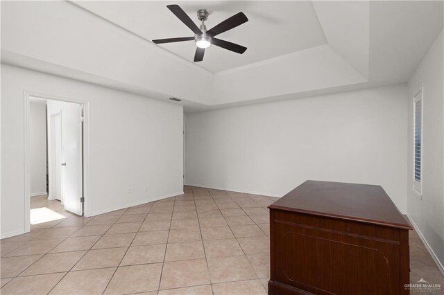 spare room with light tile patterned floors, a tray ceiling, a ceiling fan, and baseboards