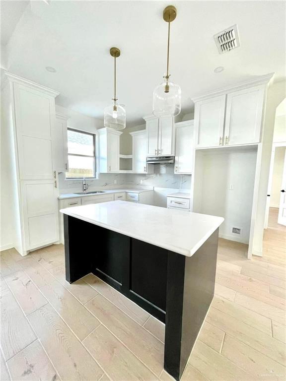 kitchen featuring a kitchen island, white cabinets, decorative light fixtures, and light wood-type flooring