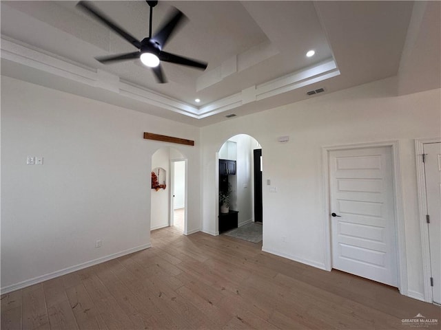 empty room with a tray ceiling, ceiling fan, and light wood-type flooring