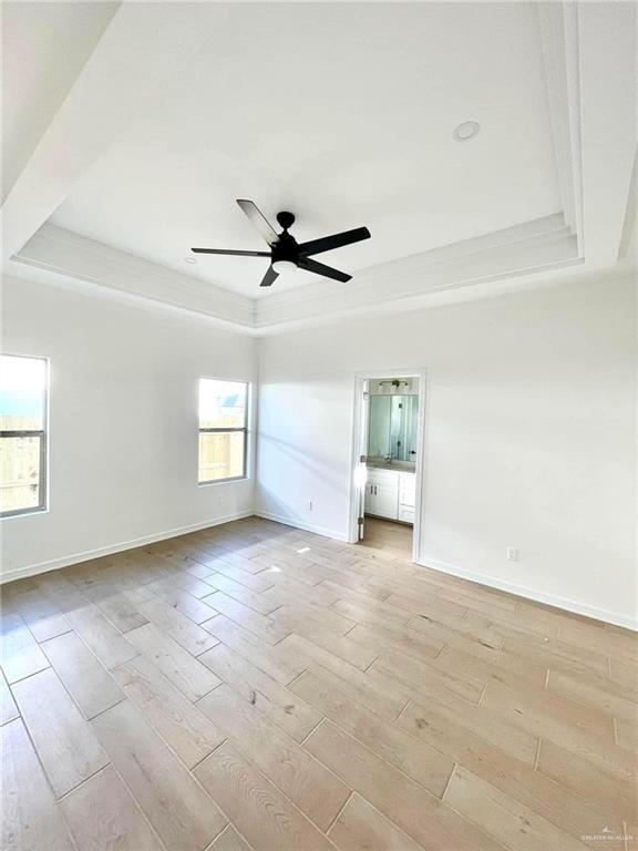 empty room featuring light hardwood / wood-style floors, ceiling fan, and a tray ceiling