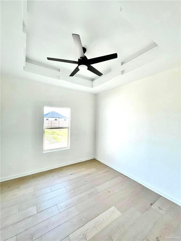 empty room with a tray ceiling, ceiling fan, and light hardwood / wood-style floors