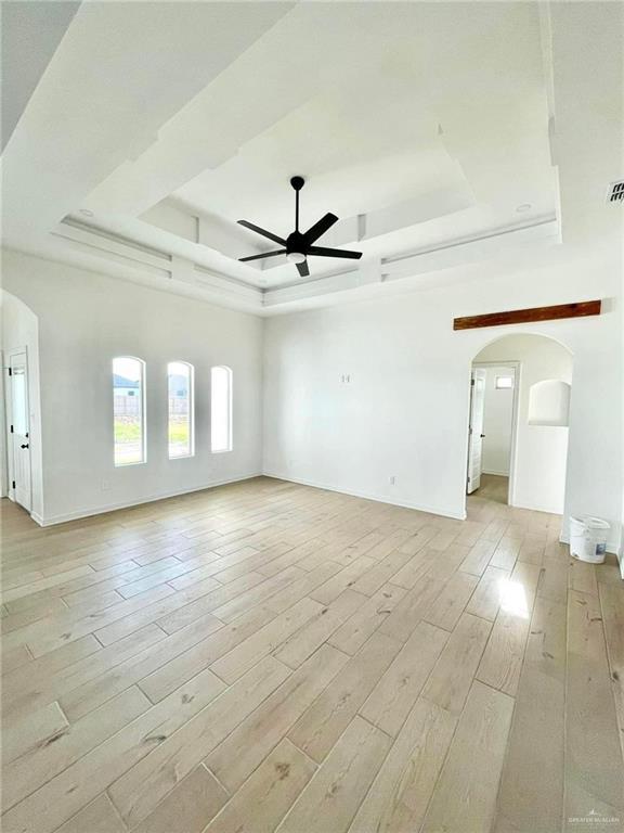 unfurnished room with a tray ceiling, ceiling fan, and light wood-type flooring