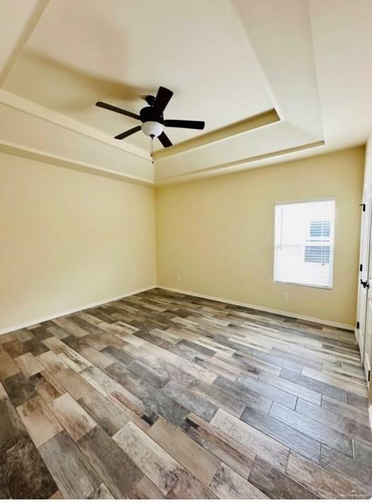 spare room with a raised ceiling, ceiling fan, and wood-type flooring