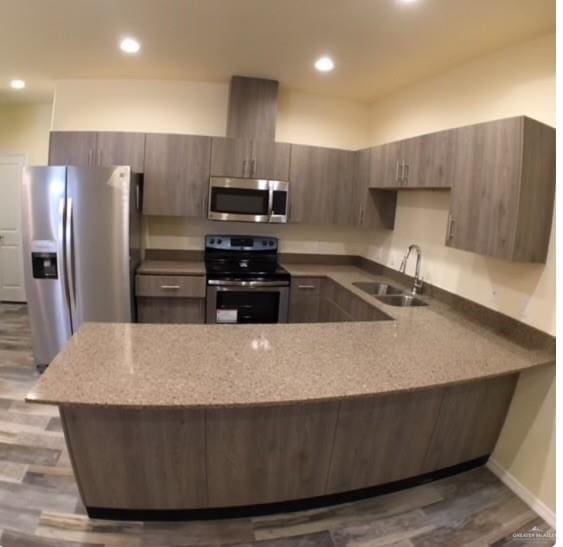 kitchen with kitchen peninsula, appliances with stainless steel finishes, light wood-type flooring, light stone counters, and sink