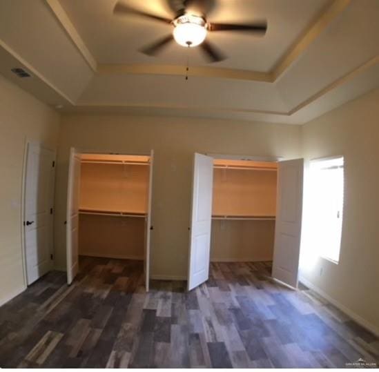 unfurnished bedroom with dark hardwood / wood-style floors, ceiling fan, and a raised ceiling