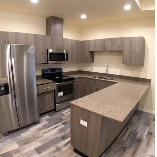 kitchen featuring kitchen peninsula, appliances with stainless steel finishes, light stone counters, dark wood-type flooring, and sink