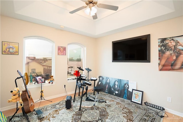 exercise room with ceiling fan, a raised ceiling, and baseboards