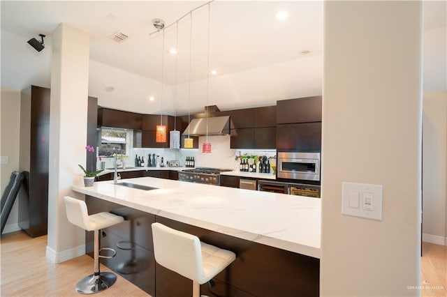 kitchen with stainless steel appliances, a sink, a kitchen bar, wall chimney range hood, and modern cabinets