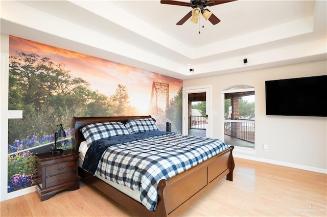 bedroom featuring light wood-type flooring, a raised ceiling, baseboards, and access to outside