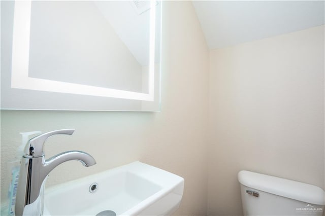 bathroom with vaulted ceiling, toilet, and a sink