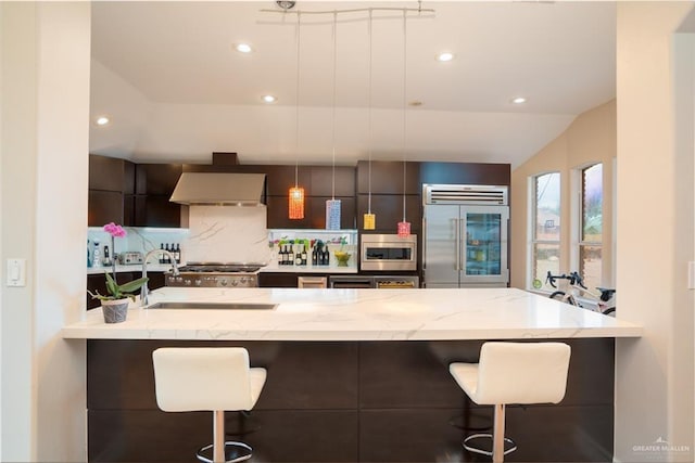 kitchen with a sink, built in appliances, a kitchen breakfast bar, wall chimney exhaust hood, and modern cabinets