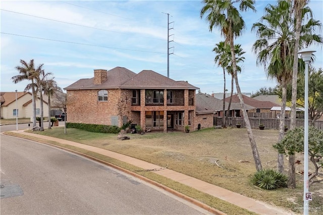 view of front facade featuring a front yard, a balcony, and brick siding