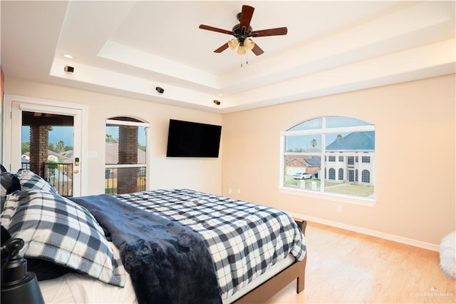 bedroom featuring ceiling fan, baseboards, light wood-type flooring, a raised ceiling, and access to outside