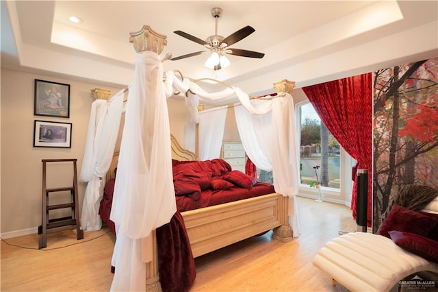 bedroom featuring a ceiling fan, wood finished floors, baseboards, a raised ceiling, and access to outside