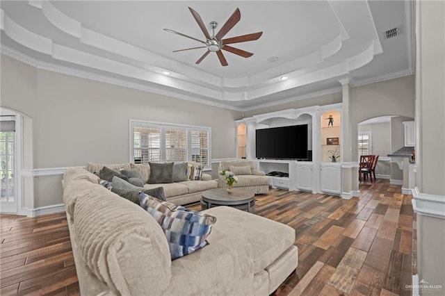 living room featuring dark hardwood / wood-style floors, ceiling fan, ornamental molding, and a tray ceiling