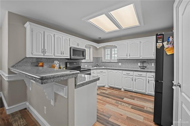 kitchen featuring light hardwood / wood-style flooring, kitchen peninsula, a breakfast bar, white cabinets, and appliances with stainless steel finishes