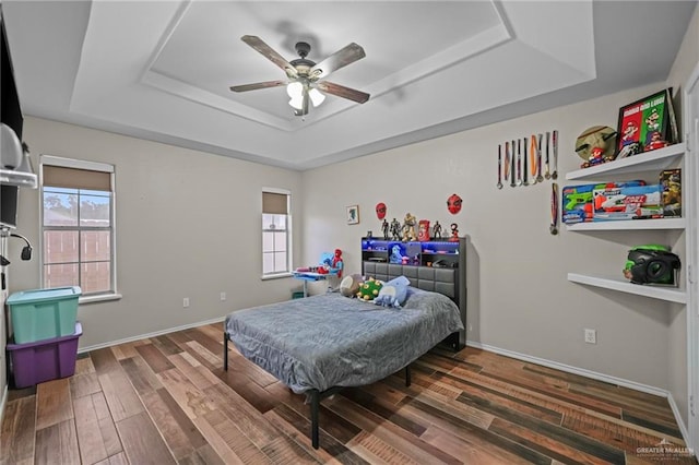 bedroom with ceiling fan, dark hardwood / wood-style flooring, and a tray ceiling