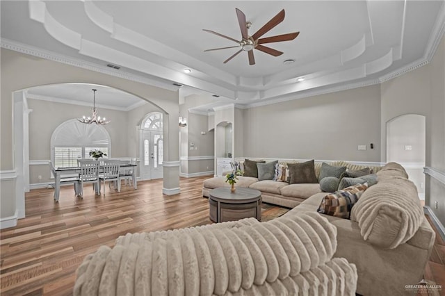 living room featuring a raised ceiling, ornamental molding, ceiling fan with notable chandelier, and hardwood / wood-style flooring