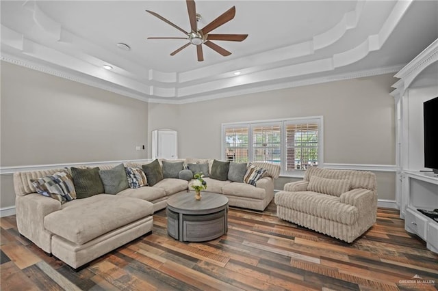 living room with a tray ceiling, ceiling fan, dark wood-type flooring, and ornamental molding