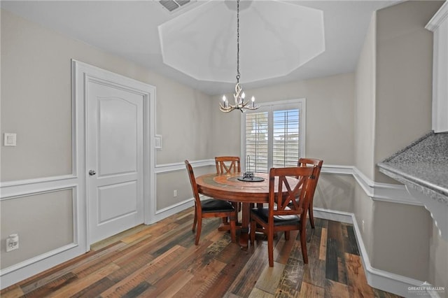 dining room with a tray ceiling, dark wood-type flooring, and a notable chandelier