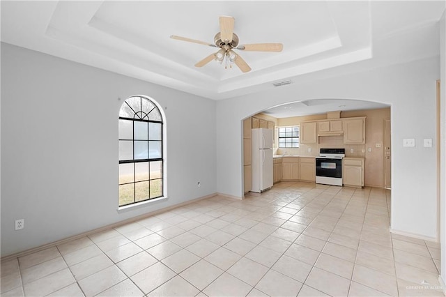 unfurnished living room featuring ceiling fan, a tray ceiling, and light tile patterned floors