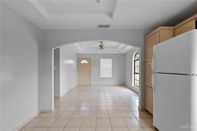 kitchen with light tile patterned flooring, light brown cabinetry, white fridge, ceiling fan, and a tray ceiling