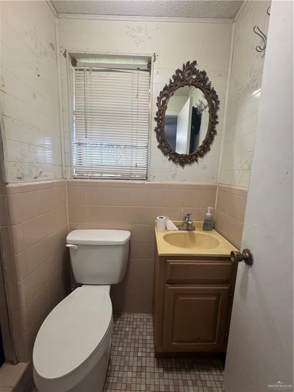 1008 S 3rd St, Edinburg, TX 78539 - half bathroom featuring vanity, a textured ceiling, wainscoting, and tile walls