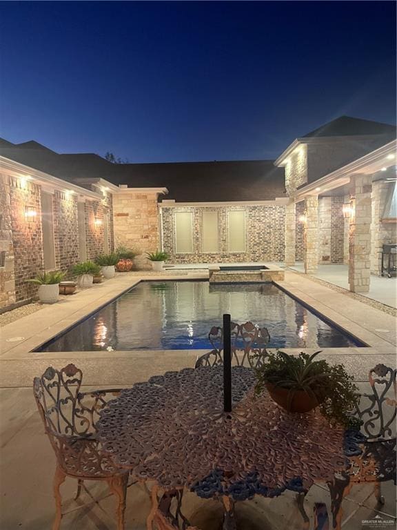 pool at twilight with an in ground hot tub and a patio