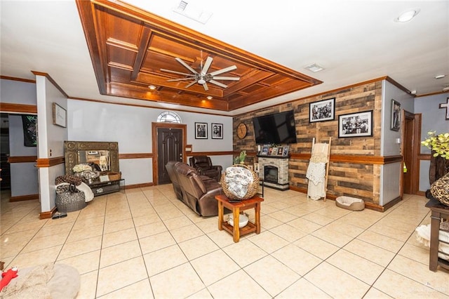 tiled living room with a fireplace, a raised ceiling, ceiling fan, and crown molding